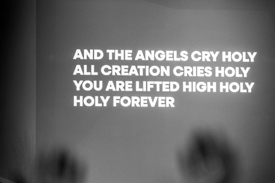 Hands raised in worship in front of a lit stage with song lyrics on the screen